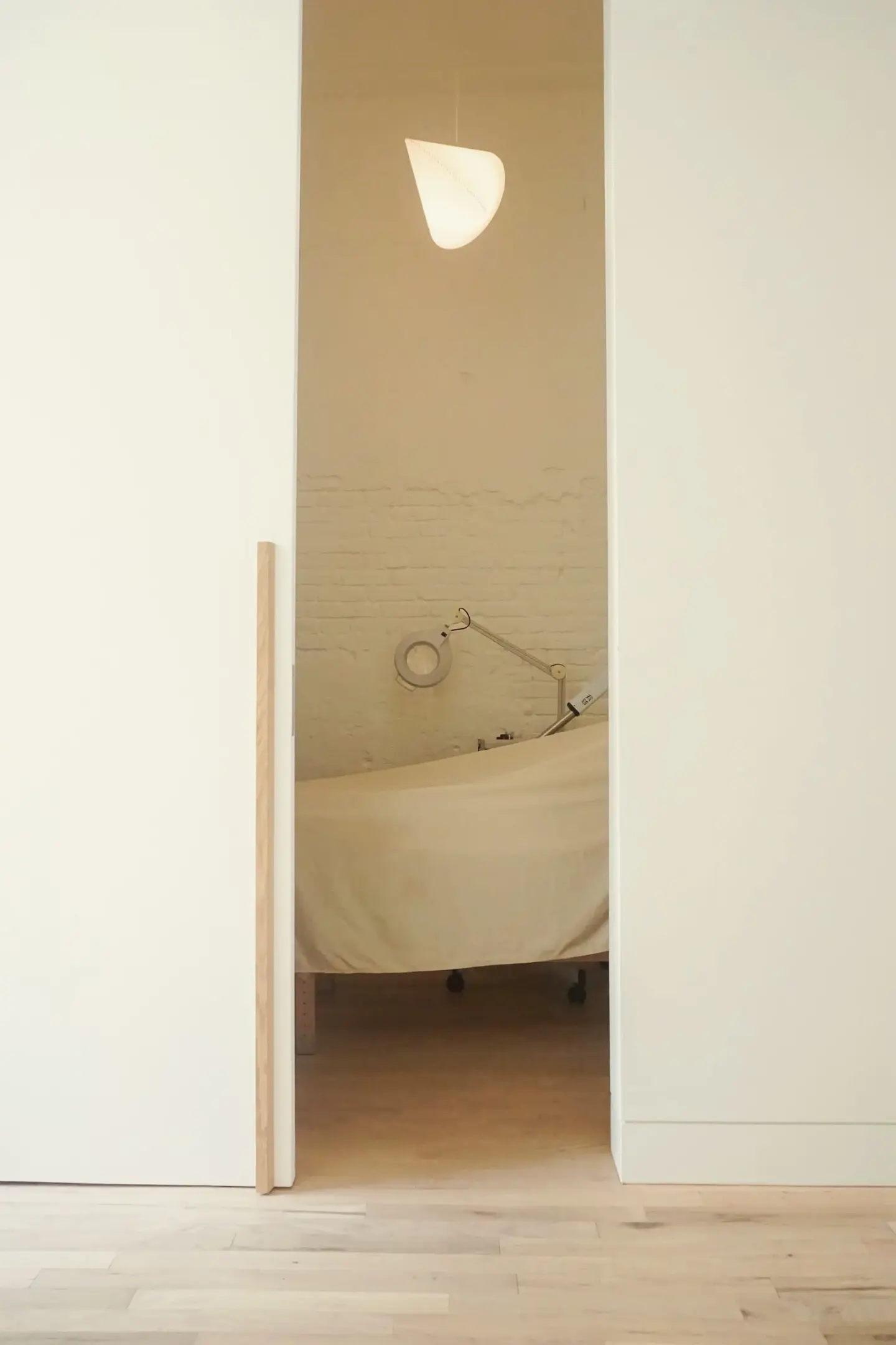 A doorway opening onto a white facial treatment room with a pendant lamp